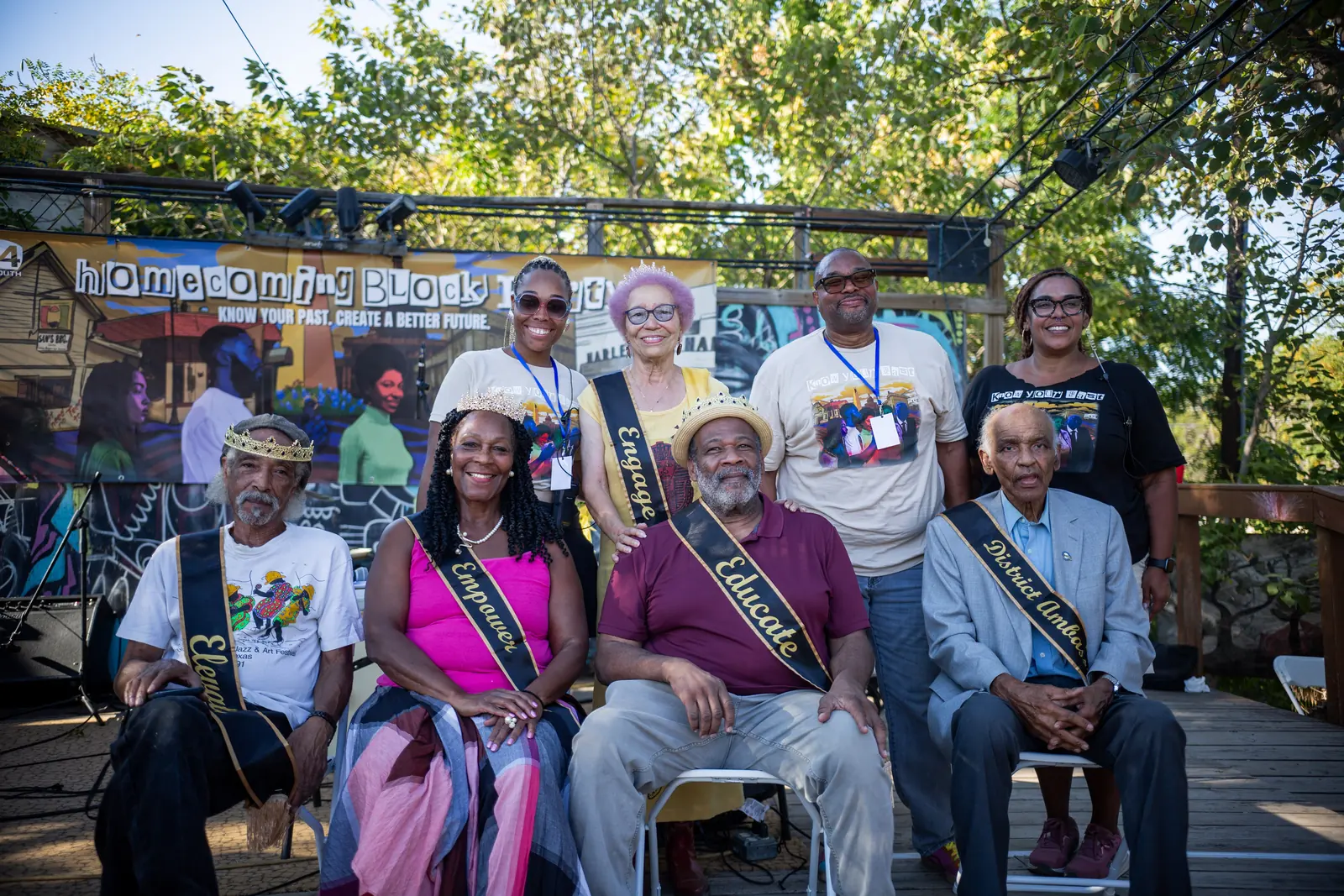 Community elders and E4 Youth supporters posing in front of a Homecoming Block Party mural that reads Know Your Past, Create a Better Future